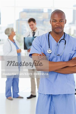 Doctor in scrubs with folded arms and two colleagues behind him