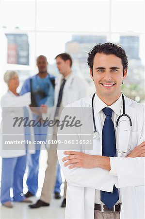 Jeune médecin avec les bras croisés et trois de ses collègues lui derrière le sourire