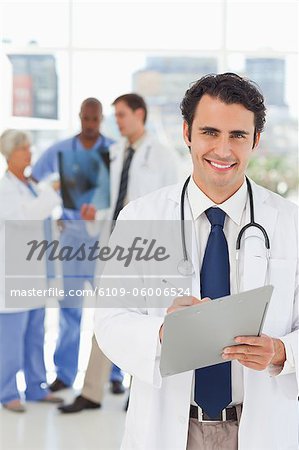 Smiling young doctor with clipboard and three colleagues behind him