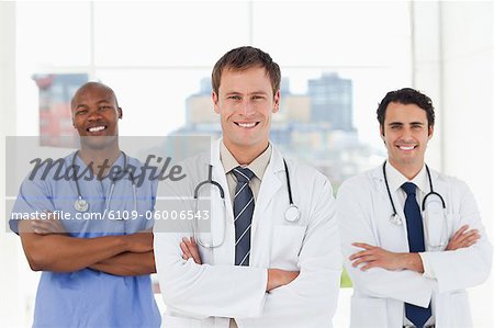 Three smiling doctors with folded arms standing in front of a window