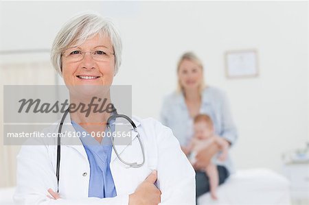 Doctor with arms crossed and woman with her little baby behind her