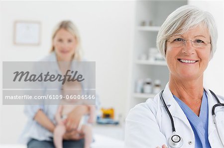 Smiling mature doctor with woman and her little baby behind her