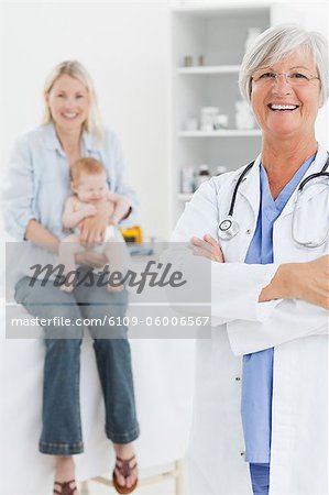 Smiling pediatrician with arms folded and mother with her little baby behind her