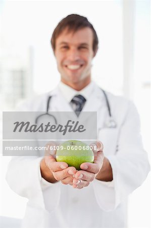 A happy doctor is holding a green apple in front of a window