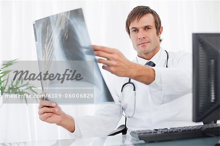 Doctor seriously holding a chest x-ray while sitting at his desk behind his computer