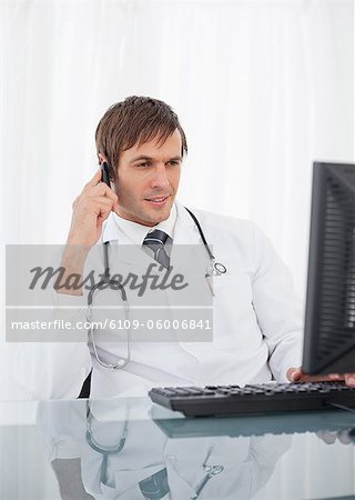 Relaxed surgeon sitting down talking on a mobile phone while looking at his computer