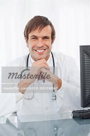 Docteur heureux assis à son bureau tout en plaçant ses mains devant son menton