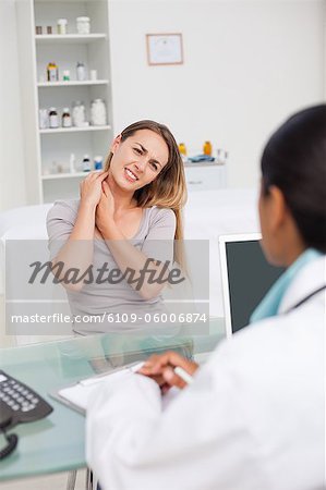 Patient placing her hands on her neck while explaining her pain to her doctor