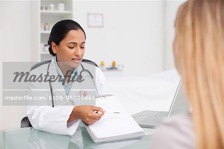 Schwere Praktiker ihre Zwischenablage mit einem Stift zeigen, während ein Patient sitzt vor
