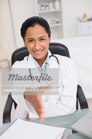 Smiling doctor offering a handshake while sitting in her medical office