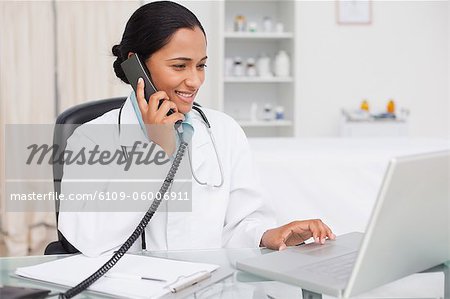Smiling practitioner looking at her laptop while talking on the phone
