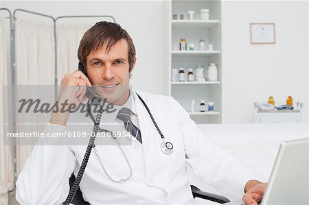 Smiling doctor talking on his phone while working on his laptop