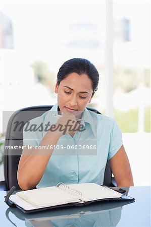 Young serious secretary looking at a binder folder while sitting at a desk