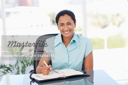 Smiling secretary looking at the camera while writing on a diary