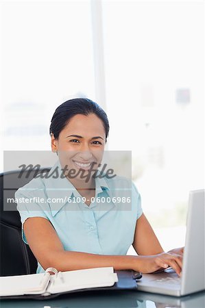 Happy secretary using her laptop while sitting at a desk and staring at the camera