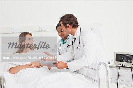 Serious doctors explaining something to a patient lying in a hospital bed