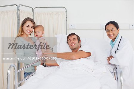 Junger Mann liegend in einem Krankenhausbett während umgeben von seiner Familie und ein Arzt