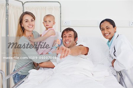 Heureux homme pointant la caméra tout en étant entouré de sa famille et un médecin