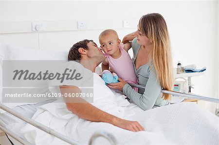 Bébé tenu par sa mère tout en étant embrassé par son père allongé dans un lit d'hôpital