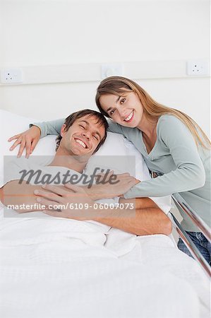 Smiling couple hugging each other while holding their hands on a hospital bed