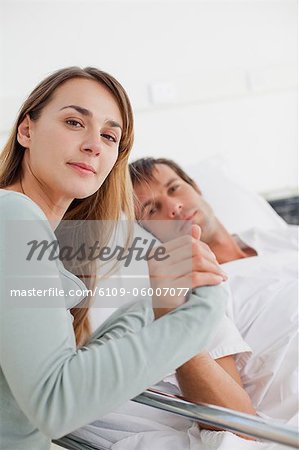 Relaxed woman sitting next to her husband in a hospital while looking at the camera