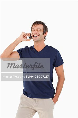 Homme heureux, à l'aide de son téléphone portable tout en riant et en plaçant sa main dans sa poche