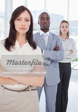 Serious man and a woman with their arms crossed standing behind their co-worker with focus on the man and woman