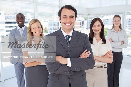 Businessman smiles as he stands in front of three women and a man who all have their arms crossed