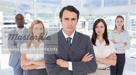 Serious businessman standing in front of two women and two men who have their arms crossed