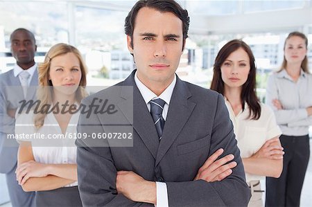 Close-up of a serious businessman standing in front of two women and two men who have their arms crossed