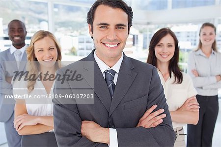 Close-up of a businessman smiles as he stands in front of three women and a man who all have their arms crossed