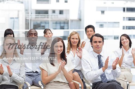 A group of colleagues look ahead and applaud as they sit next to each other