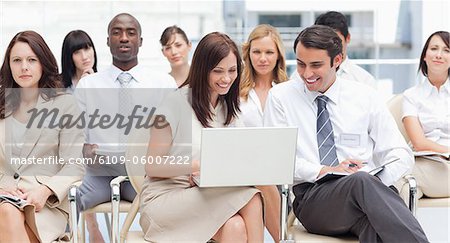 Woman looking into a laptop with her colleague as they sit in a group with other co-workers