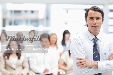 Serious businessman crossing his arms as his colleagues sit behind him