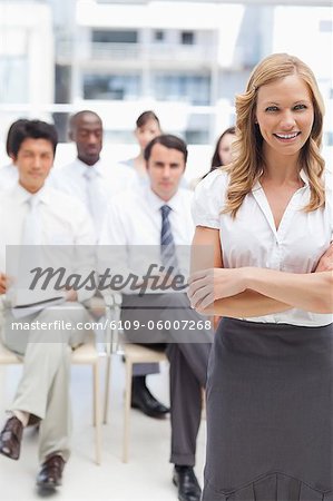 Businesswoman smiling while standing with her arms folded in front of her colleagues