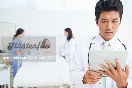 Docteur en regardant une tablette PC alors qu'un médecin et une infirmière ont à traiter un patient