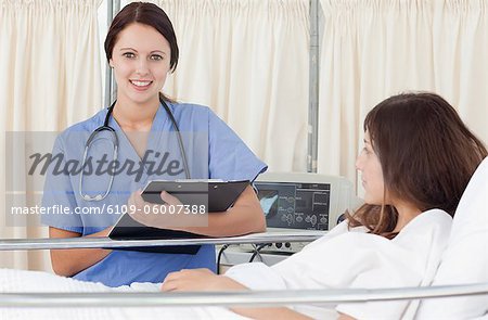 Infirmière souriante regardant en face d'elle tout en maintenant un presse-papiers à côté du lit d'un patient