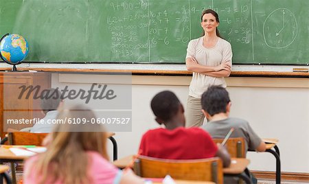 Elementary teacher with arms folded next to blackboard