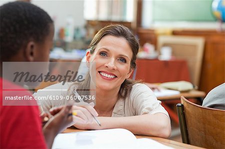 Smiling elementary teacher kneeling next to one of her students desk