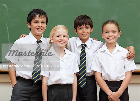 Smiling young schoolfellows in school uniforms standing in front of blackboard