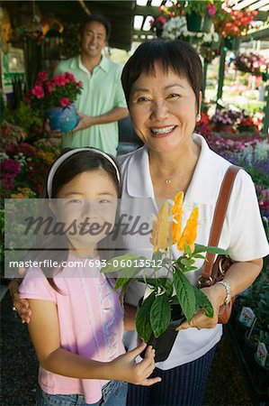 Grandmother and granddaughter in plant nursery holding flowers, portrait