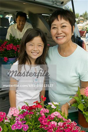 Grandmother and granddaughter with flowers by back of SUV, portrait