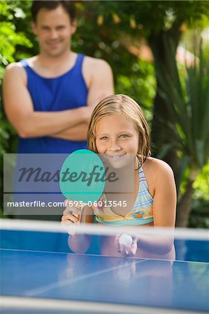 Girl (7-9) spielen Tischtennis mit Vater im Hintergrund.