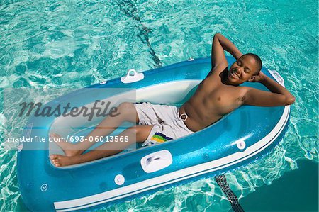 Garçon (13-15) relaxante sur radeau pneumatique dans la piscine, vue surélevée.