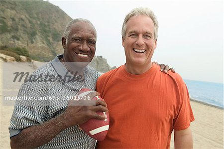 Two men with American football on beach, (portrait)