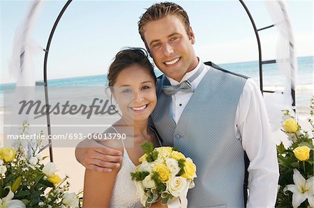 Braut und Bräutigam unter Torbogen am Strand (Hochformat)