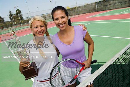 Two female Tennis Players by net on court holding trophy, portrait