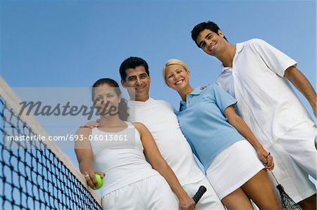 Four mixed doubles tennis players at net on tennis court, portrait, low angle view
