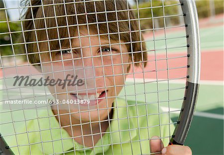 Garçon à la recherche à travers une raquette de Tennis, portrait, gros plan