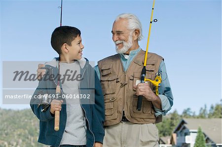 Grandfather and grandson holding fishing rods outdoors, smiling